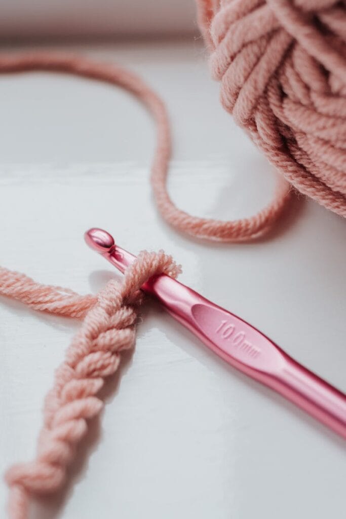 Close-up of pink yarn and crochet hook on a bright indoor windowsill, showcasing a cozy creative hobby.