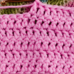 A close-up of a pink swatch a tutorial to how to learn double crochet stitches, with a crochet hook inserted into the loops of the yarn.