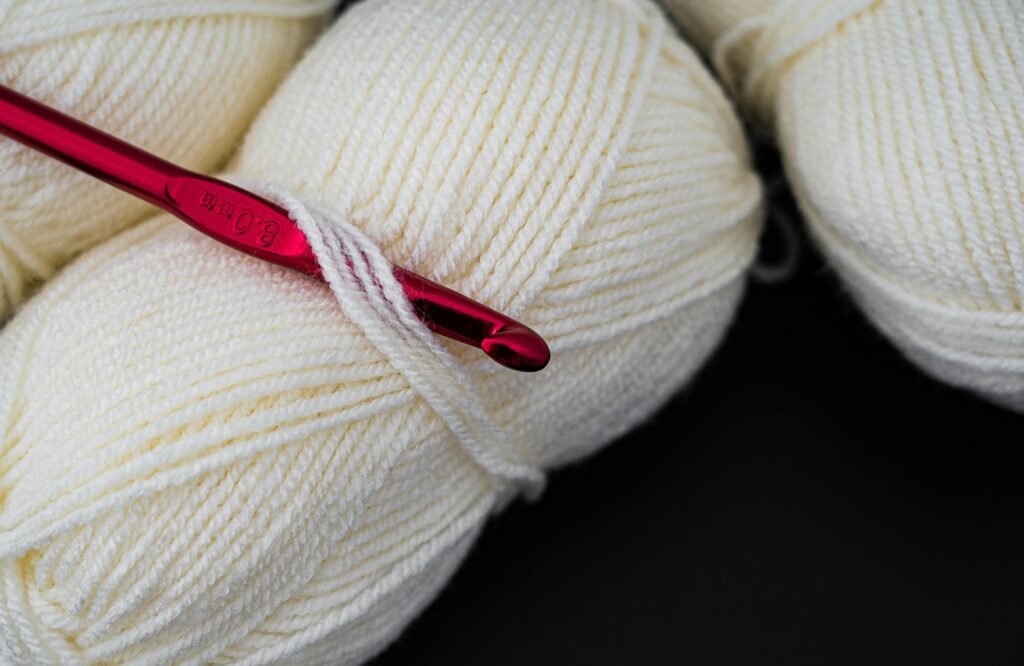 Close-up image of cream-colored yarn balls with a red crochet hook, highlighting texture and detail.