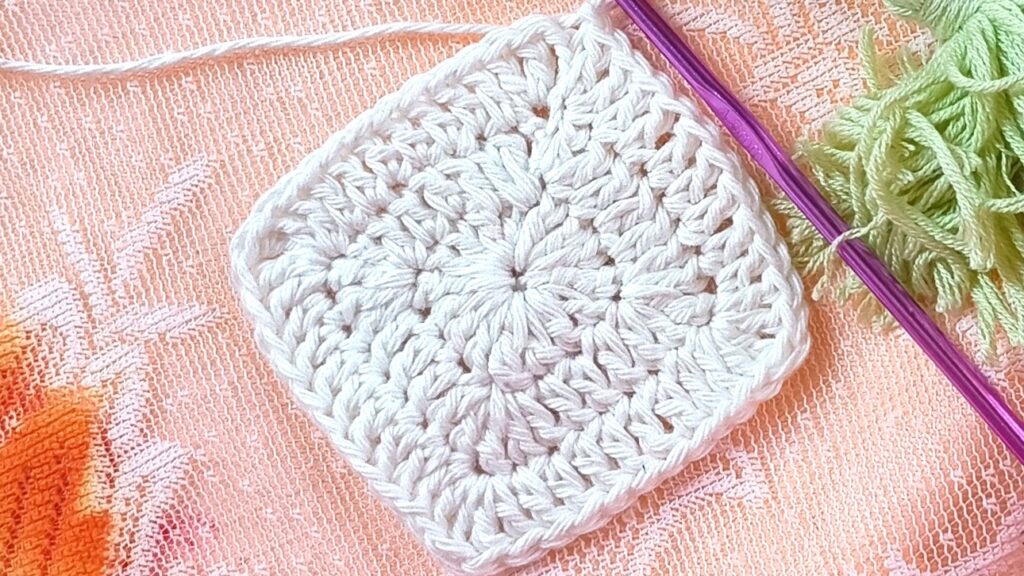 white color granny square with purple color crochet hook