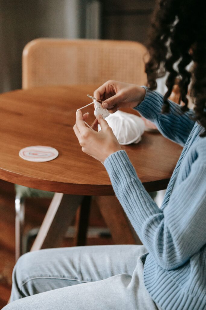 A young woman sits at a wooden table crocheting, showcasing a tranquil indoor scene.