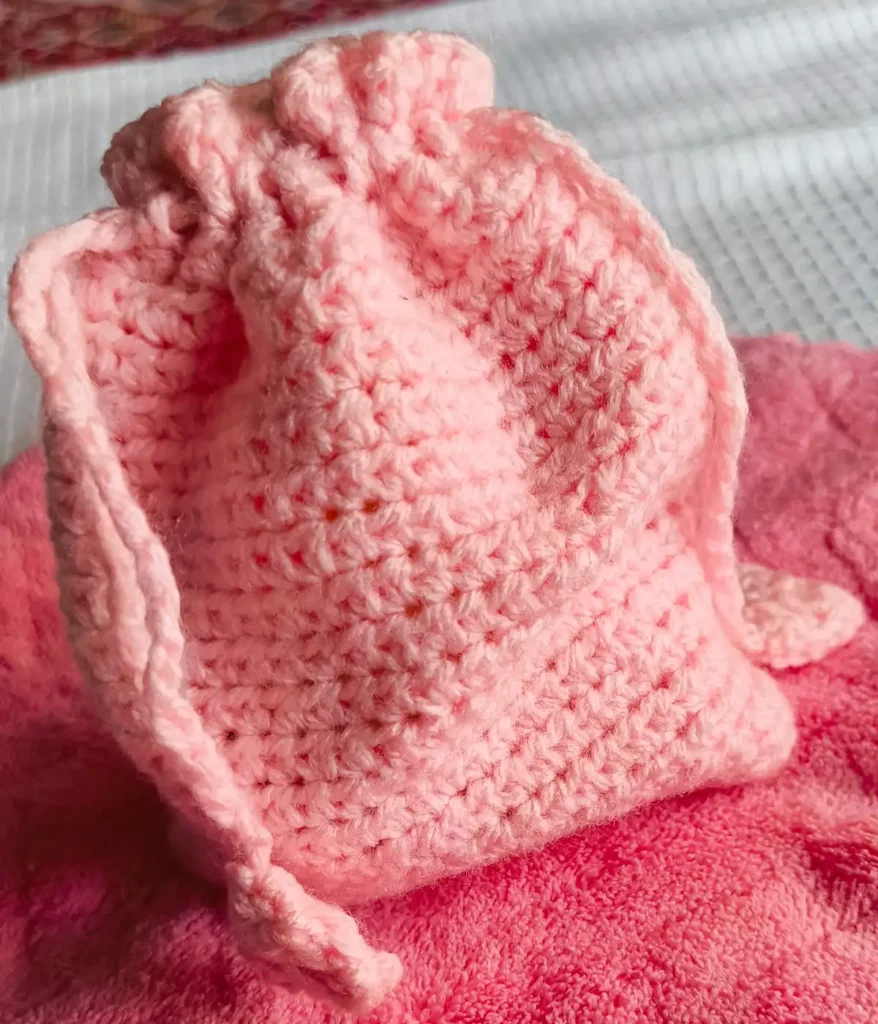 crochet-gift-bag A crochet pink bag tied with a drawstring and placed on a pink and white background.
