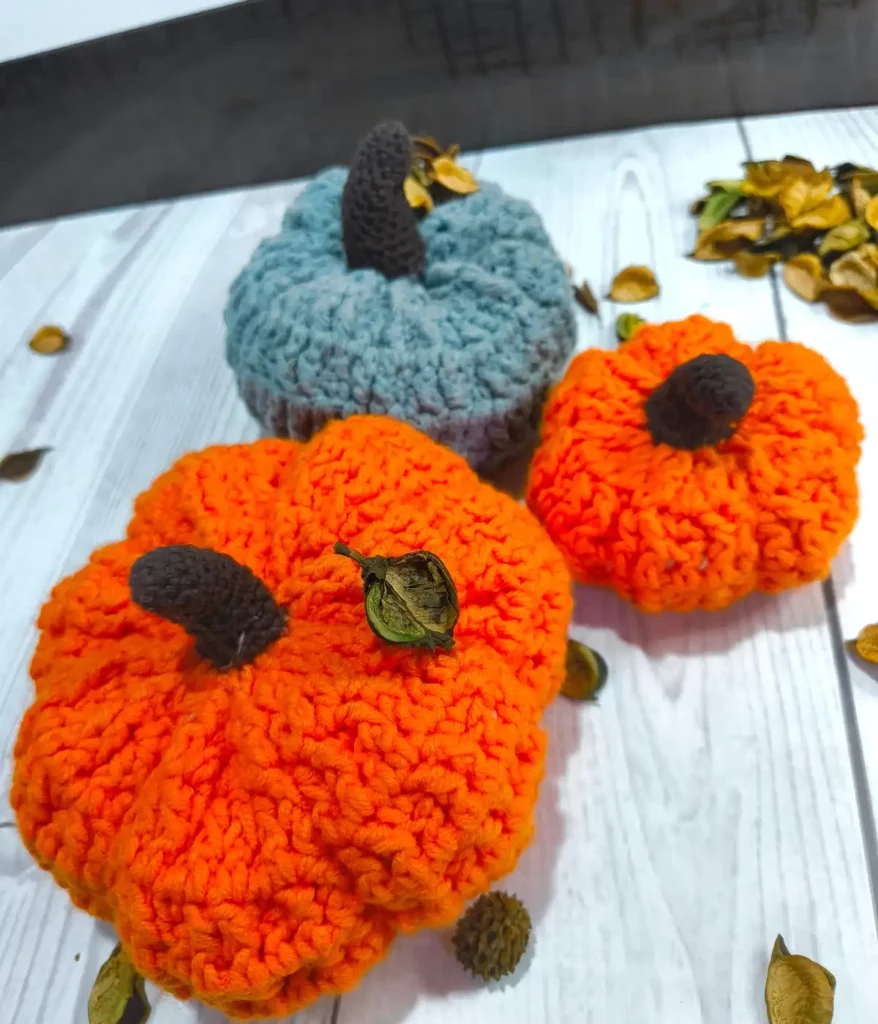 2 orange and 1 greyish pumpkins are placed together with some dried leaves on a white table