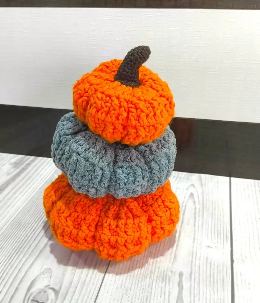 3 pumpkins are stacked on each other placed on a white table with brown and white background