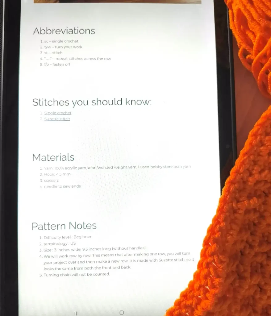 1 tablet showing a crochet pattern along with 1 crochet swatch and a yarn.