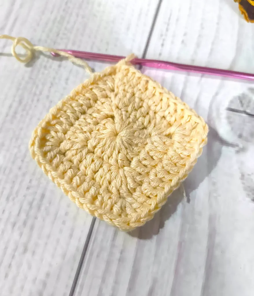 Peach color granny Square with purple color crochet hook and white wooden table background