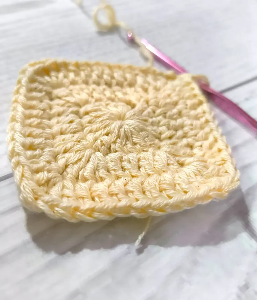 Closer look of granny Square with a crochet hook , white wooden table background