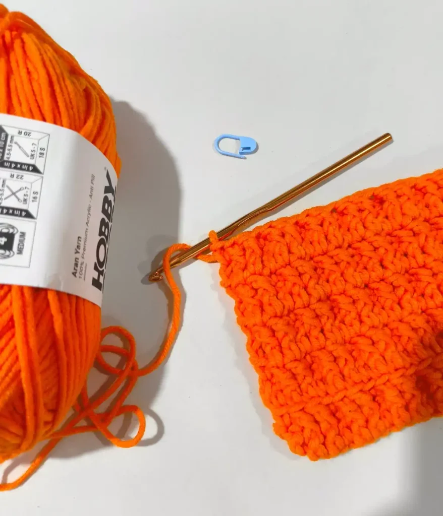 An orange color skien and a swatch of a crochet stitch with orange color crochet hook
