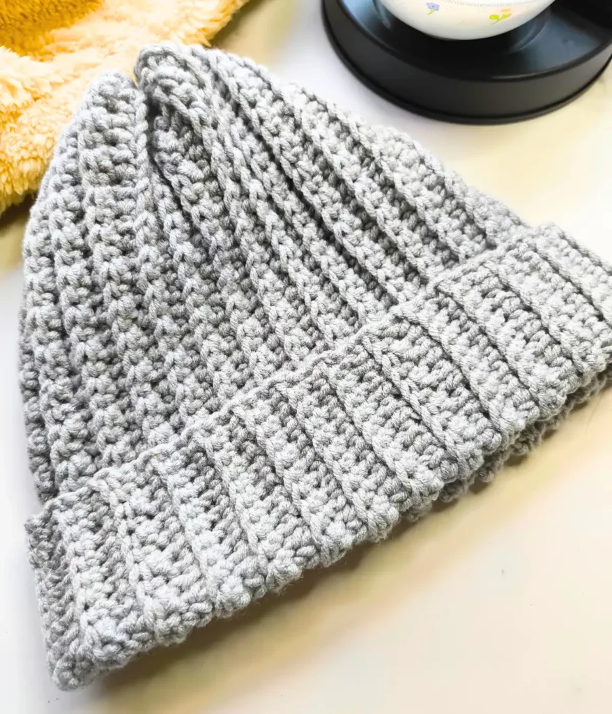 A grey coloured simple crochet hat pattern is placed on a white background