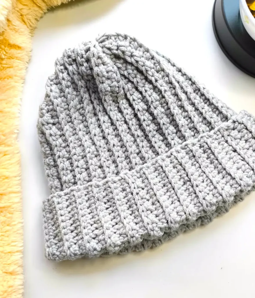 A grey coloured crocheted beanie hat is placed on a white table along with a fur and a black showpiece with a white showpiece